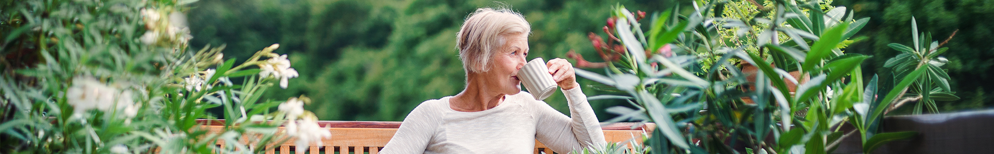 an older woman drinking coffee in a garden