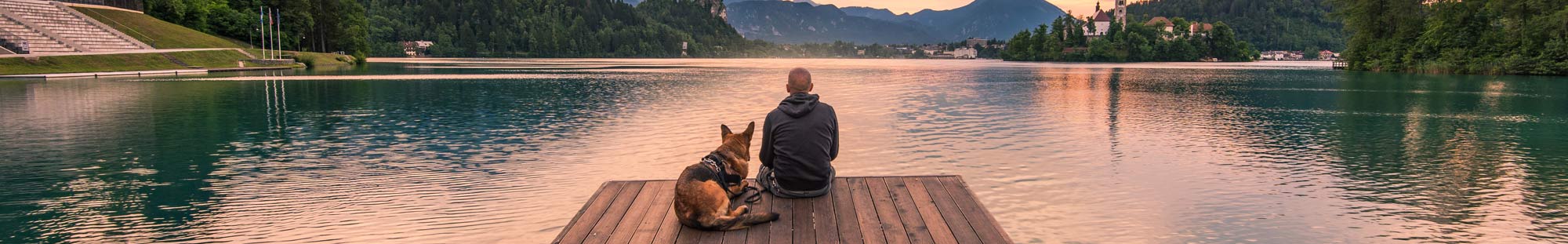 man and dog sitting on a lake dock and gazing across the water